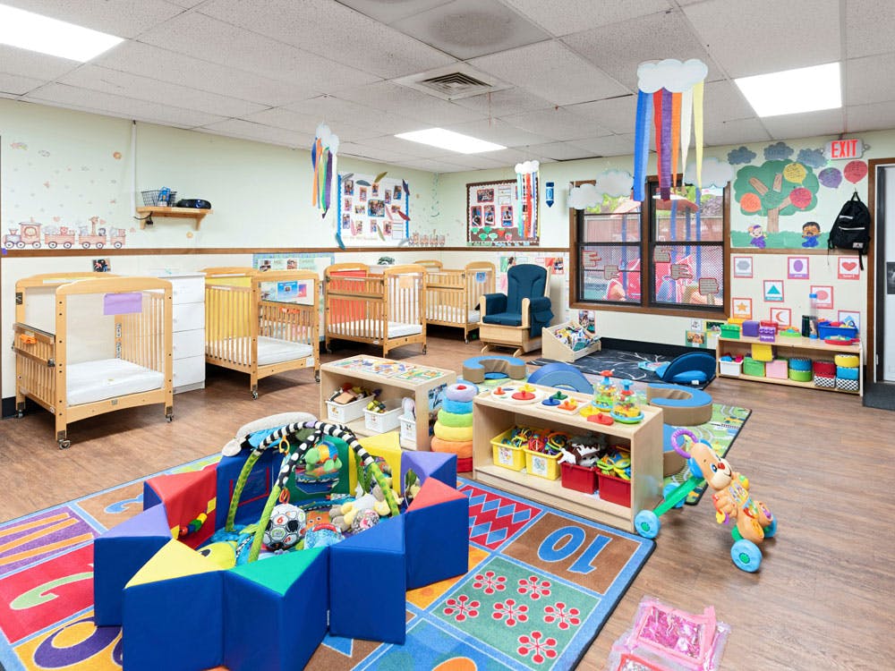 Baby room in a daycare with multiple cribs, playmats, and toys