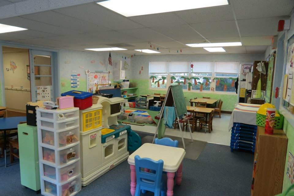 A classroom with small tables and chairs, play kitchen, and storage units