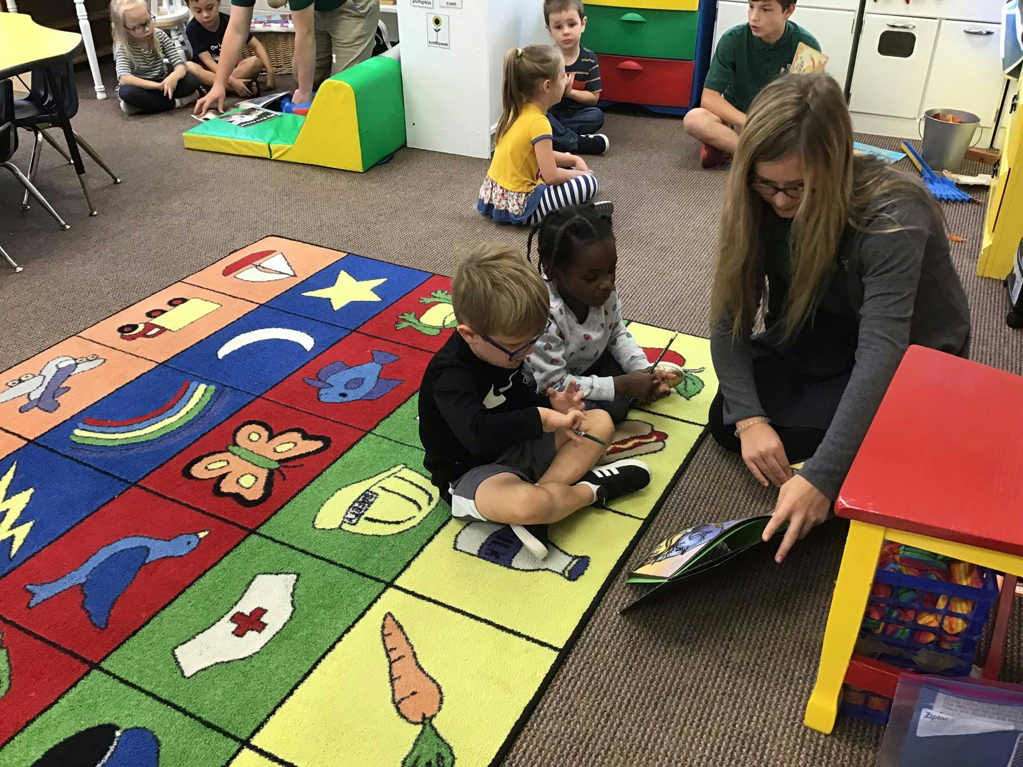 Adult reading a book to two children on a colorful rug