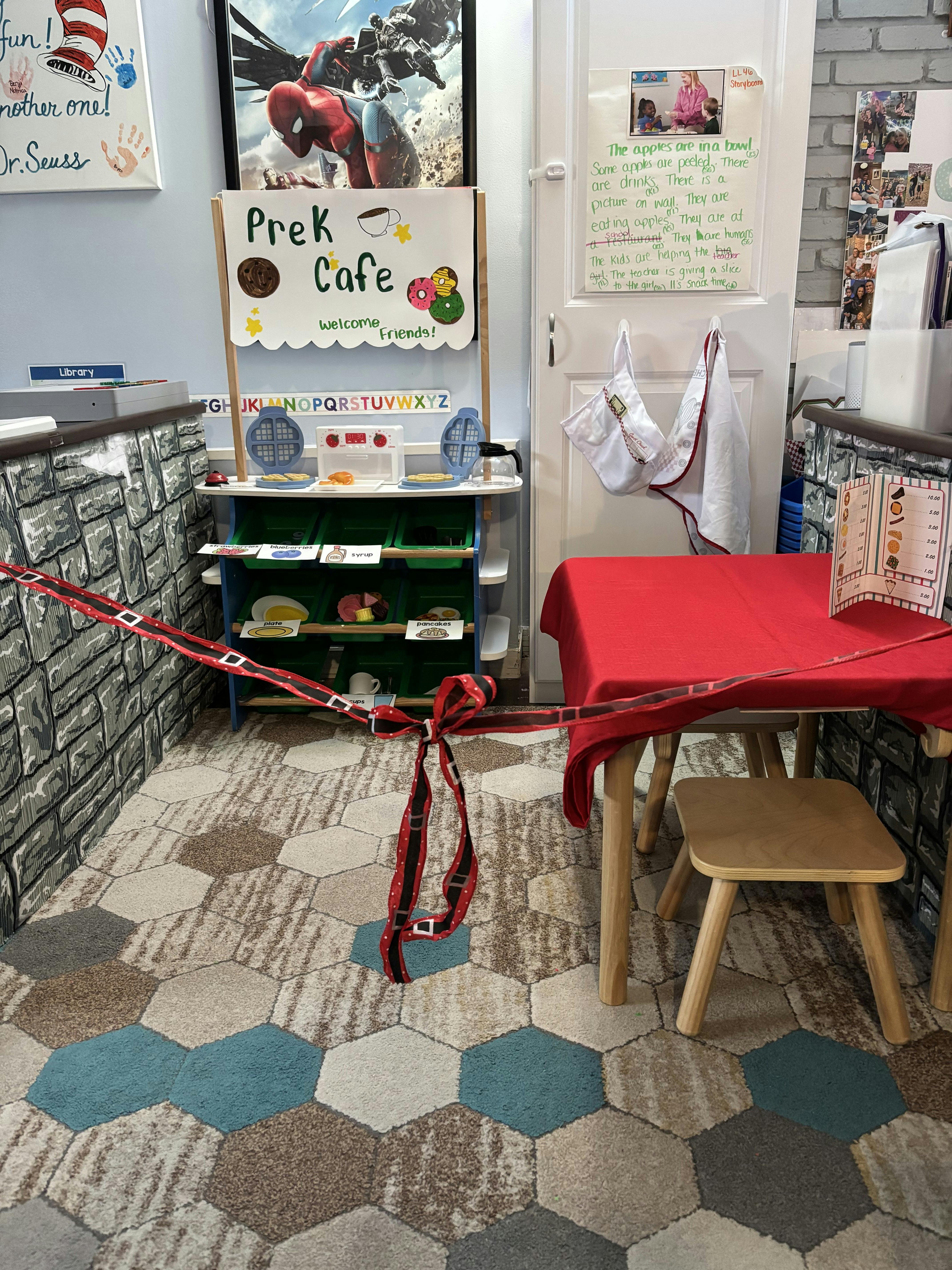 Prek Cafe sign in a classroom play area with a red tablecloth table