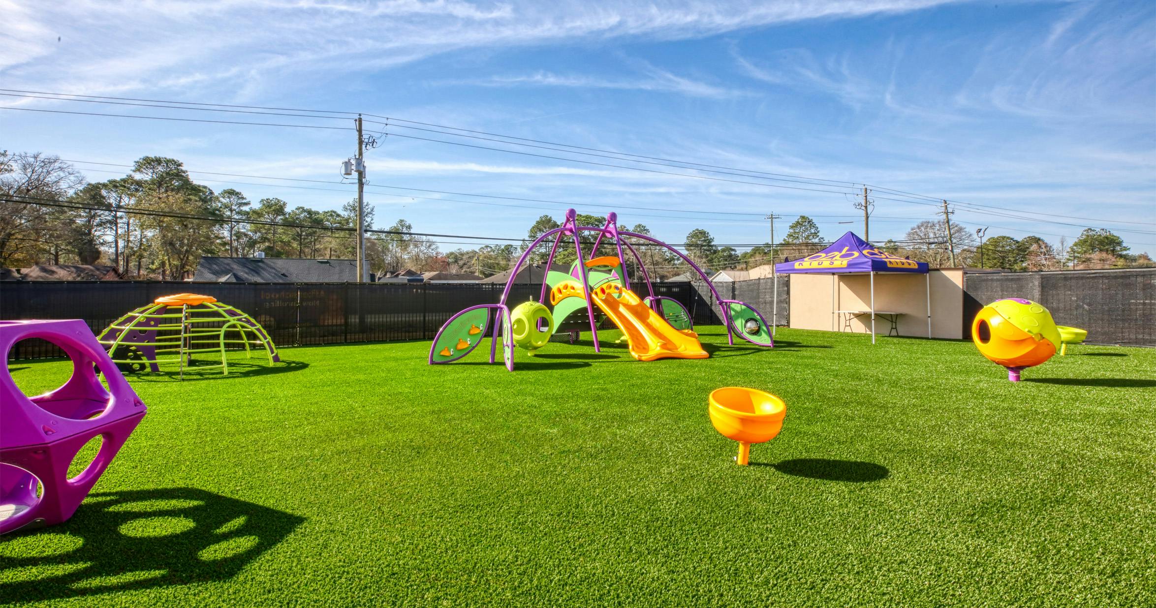Playground with green turf, purple and orange play structures, and a slide