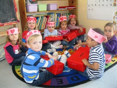Children in a classroom wearing paper crowns and holding red boxes
