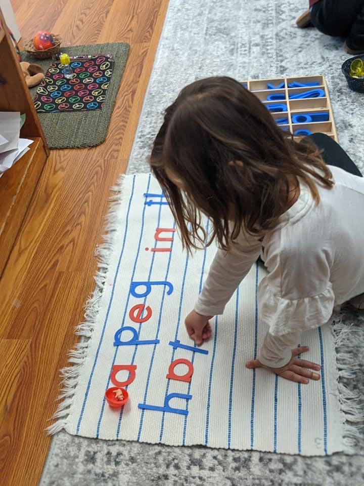 Child placing letter tiles on a mat with words "peg" and "hat"