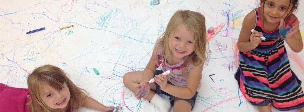 Three children drawing on a large sheet of paper