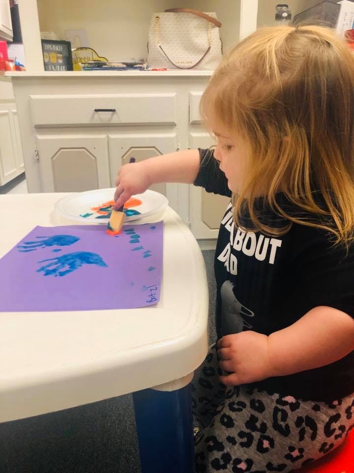 Child painting on purple paper with a sponge brush
