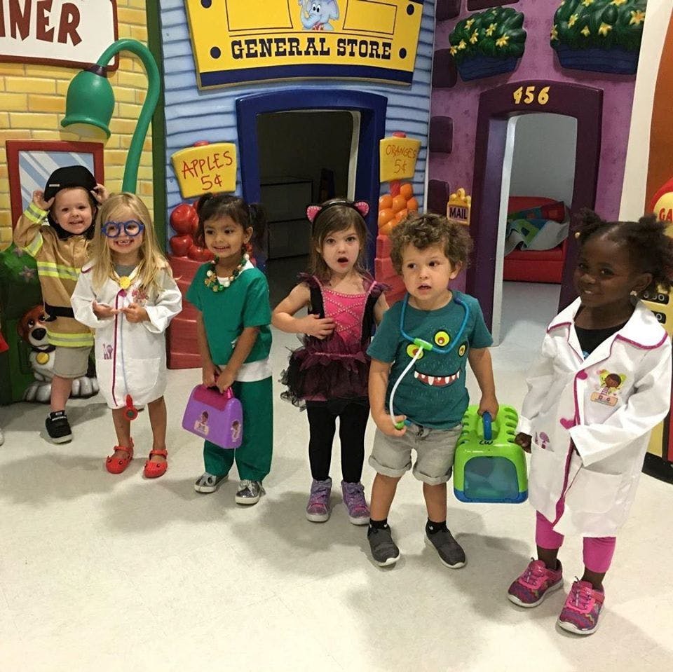 Group of children in various costumes standing in front of a play general store