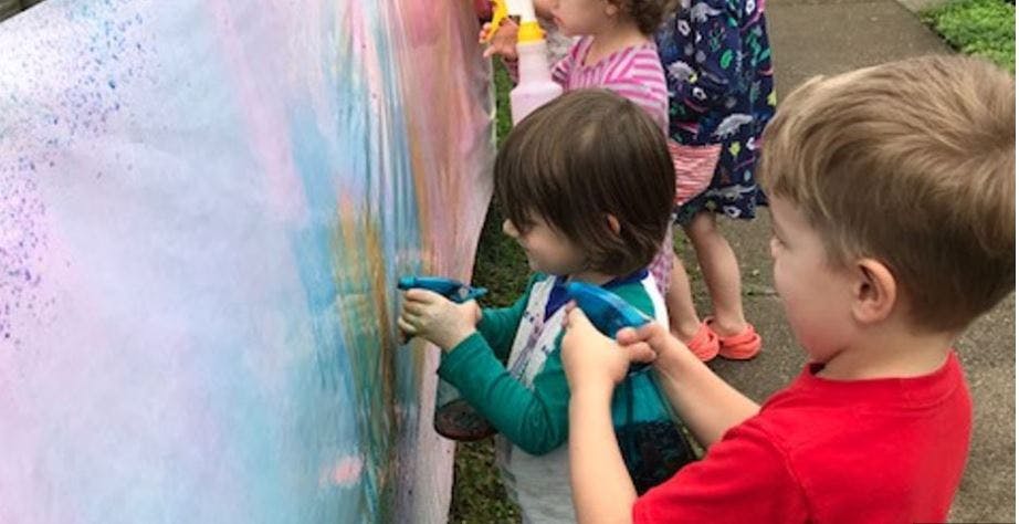 Two children spraying a colorful surface with spray bottles