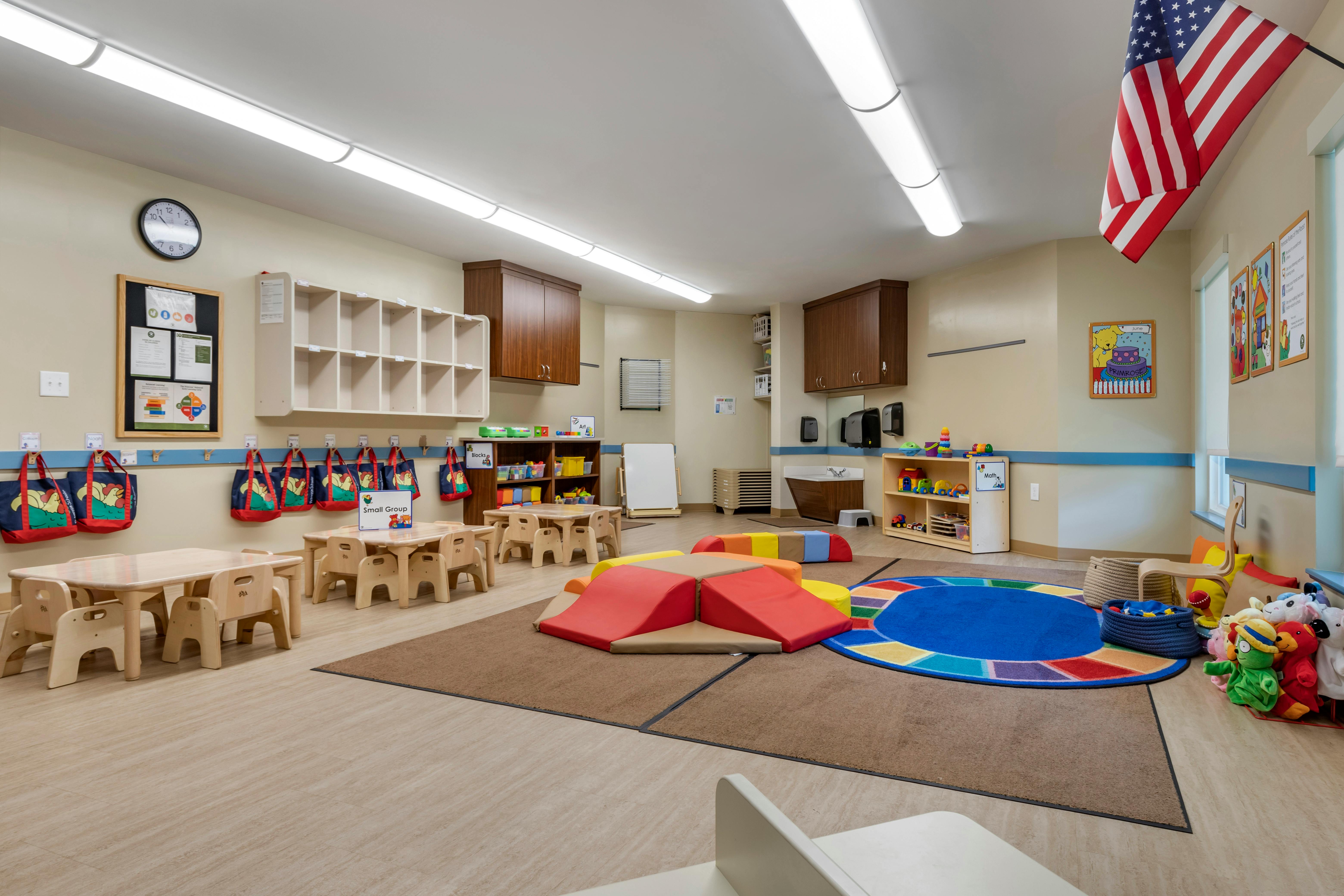 Classroom with small tables and chairs, cubbies, play mats, and toys