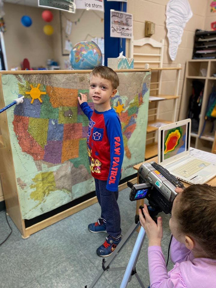 Child pointing at a map while another child films with a video camera