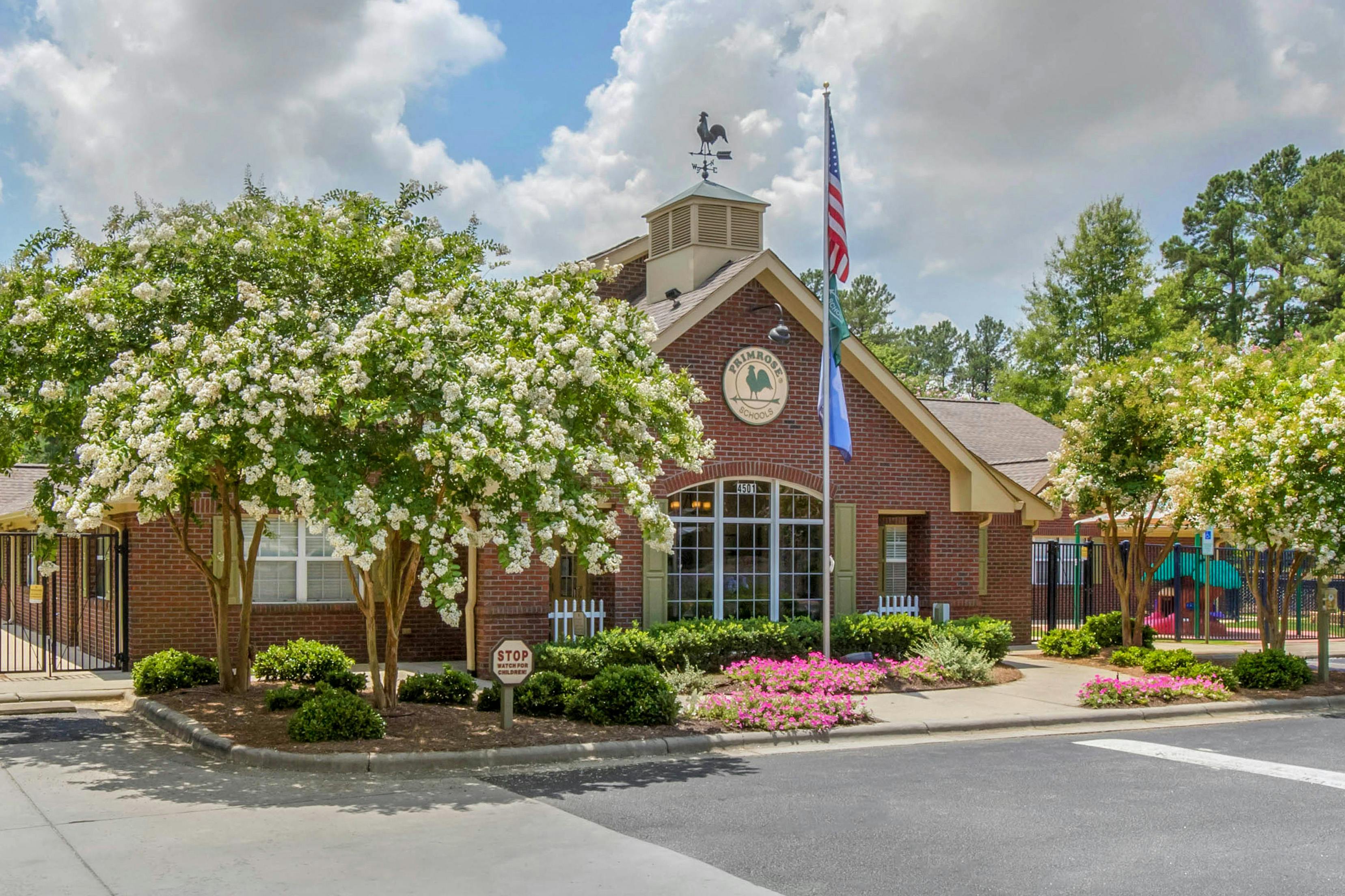 Brick building with a weather vane, flagpole, and sign for Primrose Schools