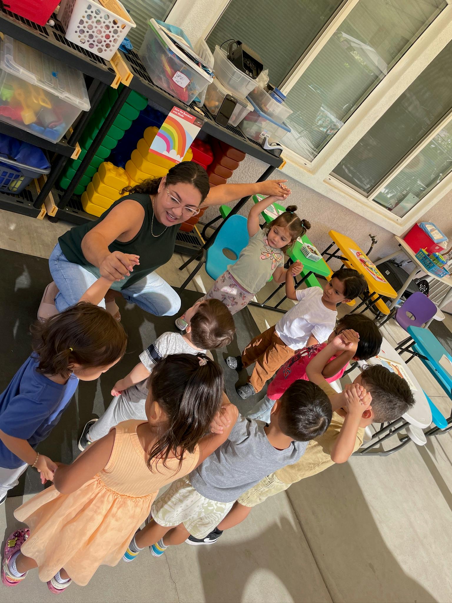Person kneeling with children in a circle, holding hands
