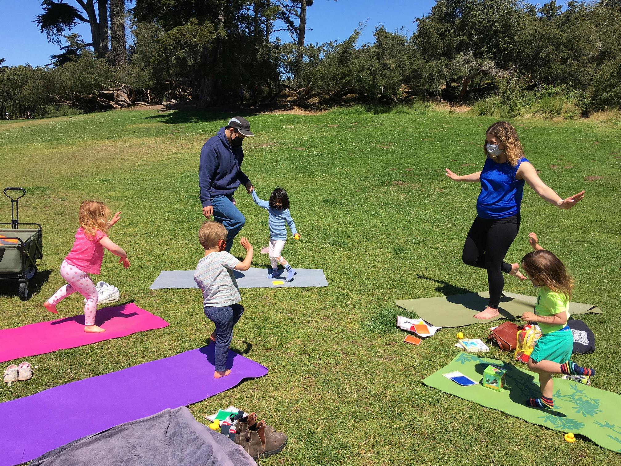 People and children doing yoga outdoors on mats