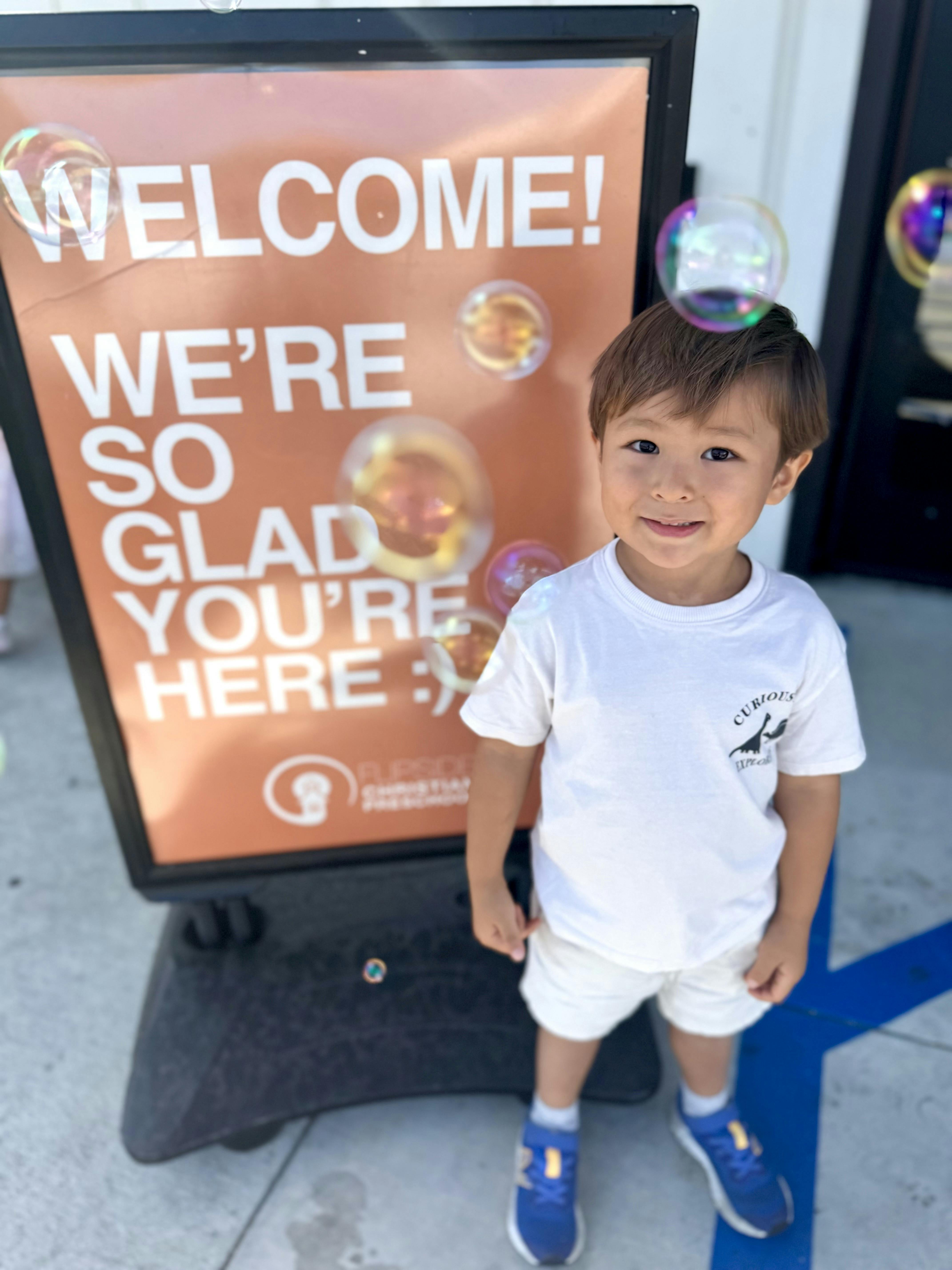 Child smiling in front of a welcome sign with floating bubbles