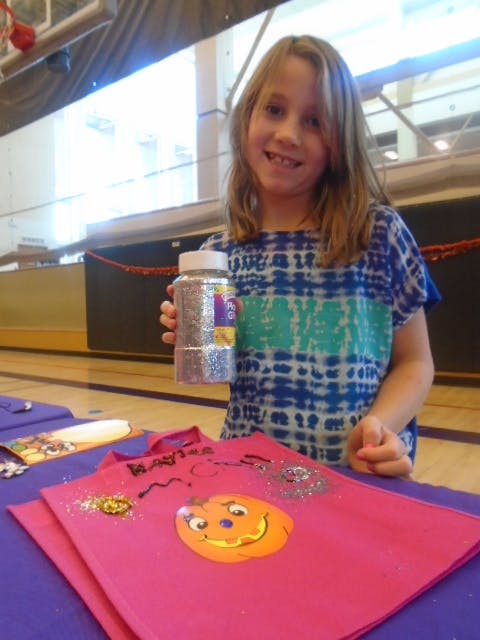 Child holding a jar of glitter next to a decorated pink shirt