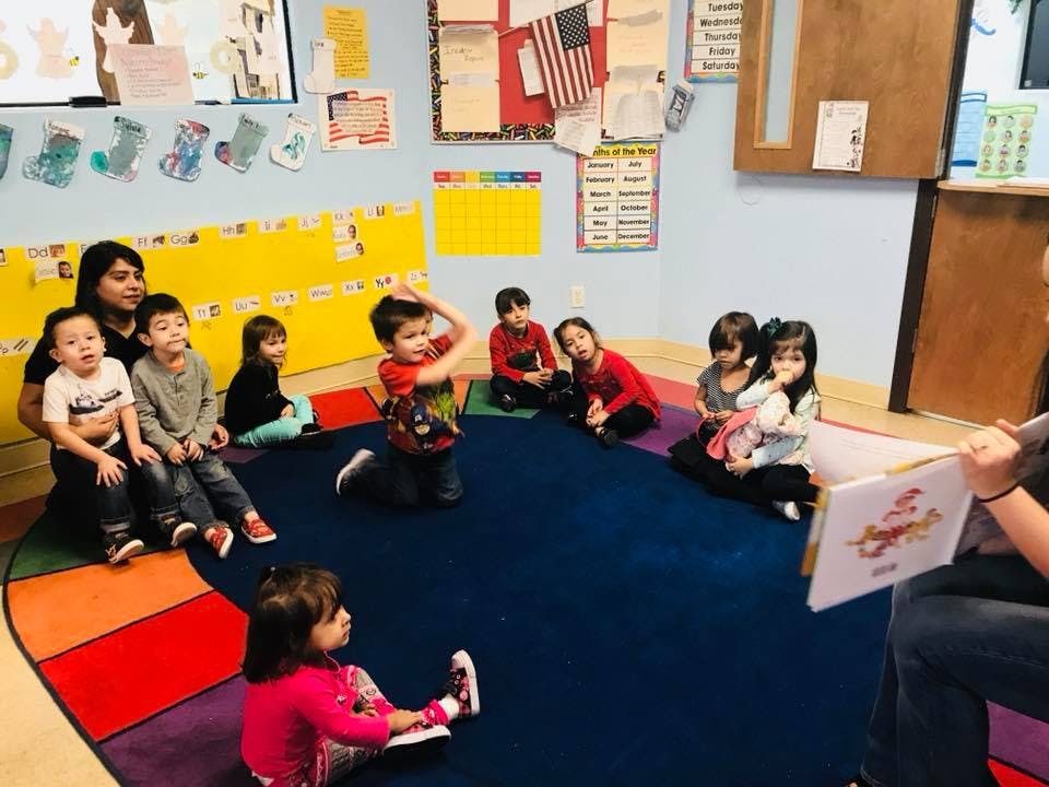 Adult reading a book to a group of children in a classroom