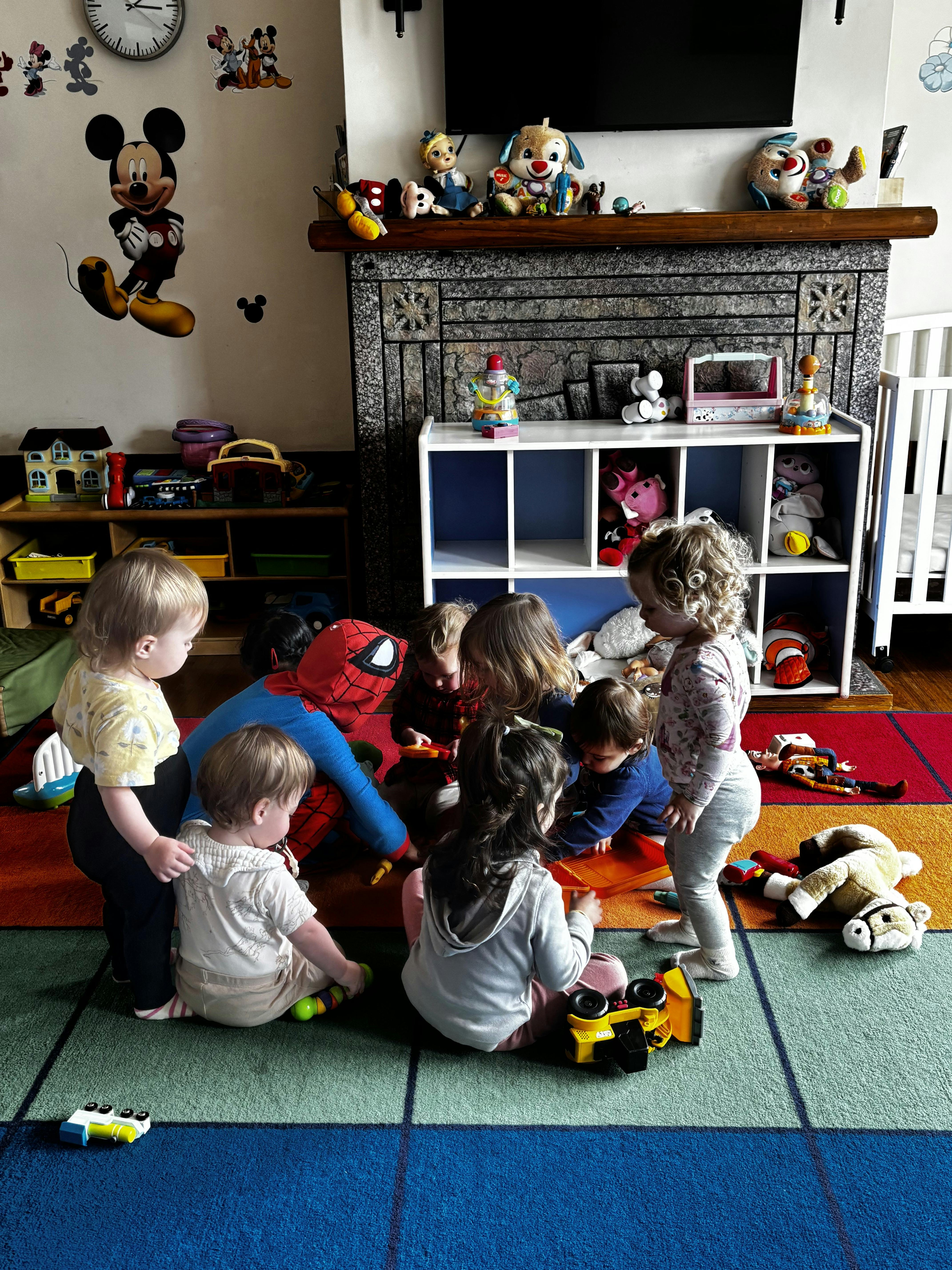 A person in a Spider-Man costume playing with a group of children on a rug