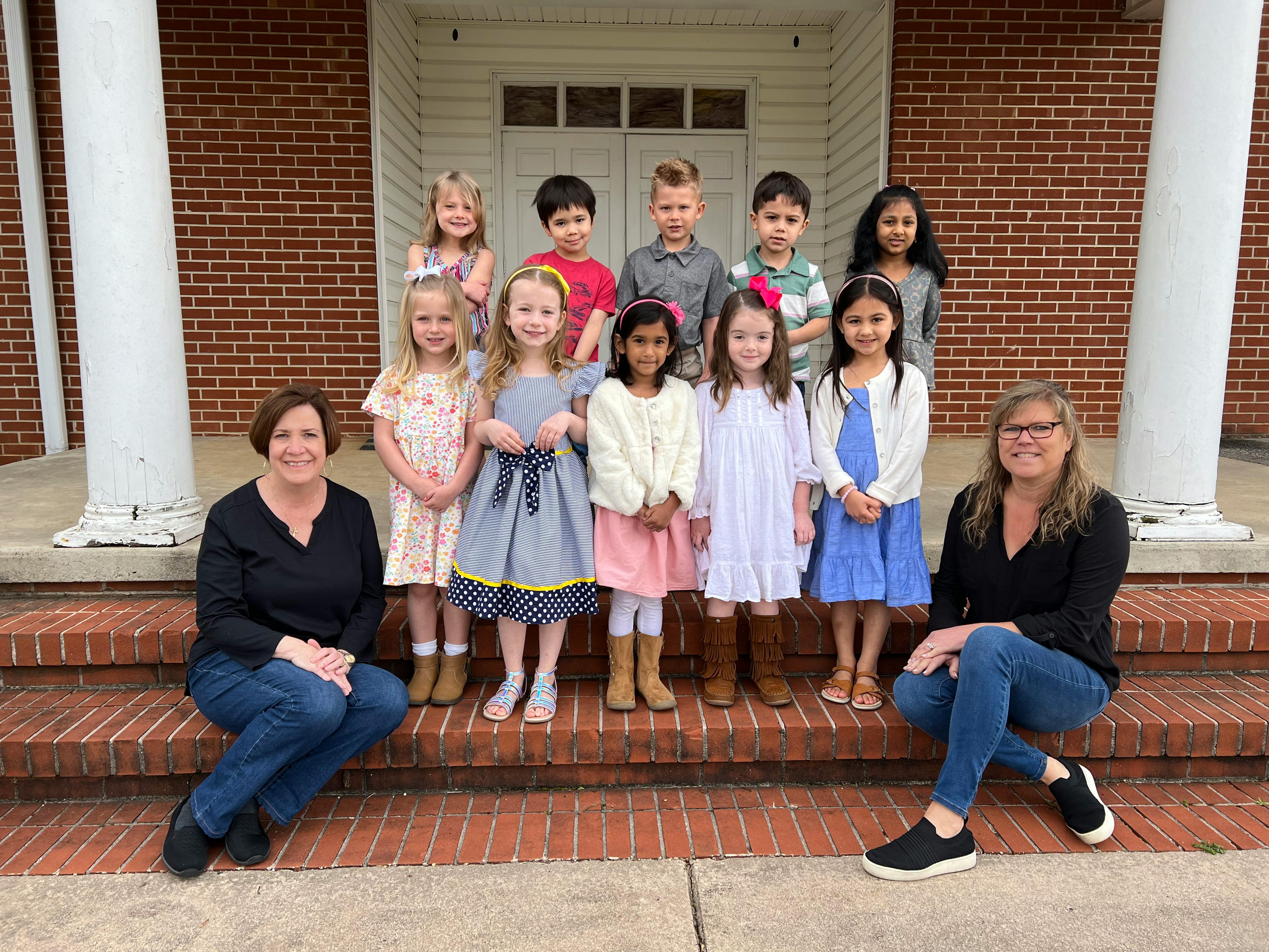 Two people sitting on steps with a group of children standing behind them