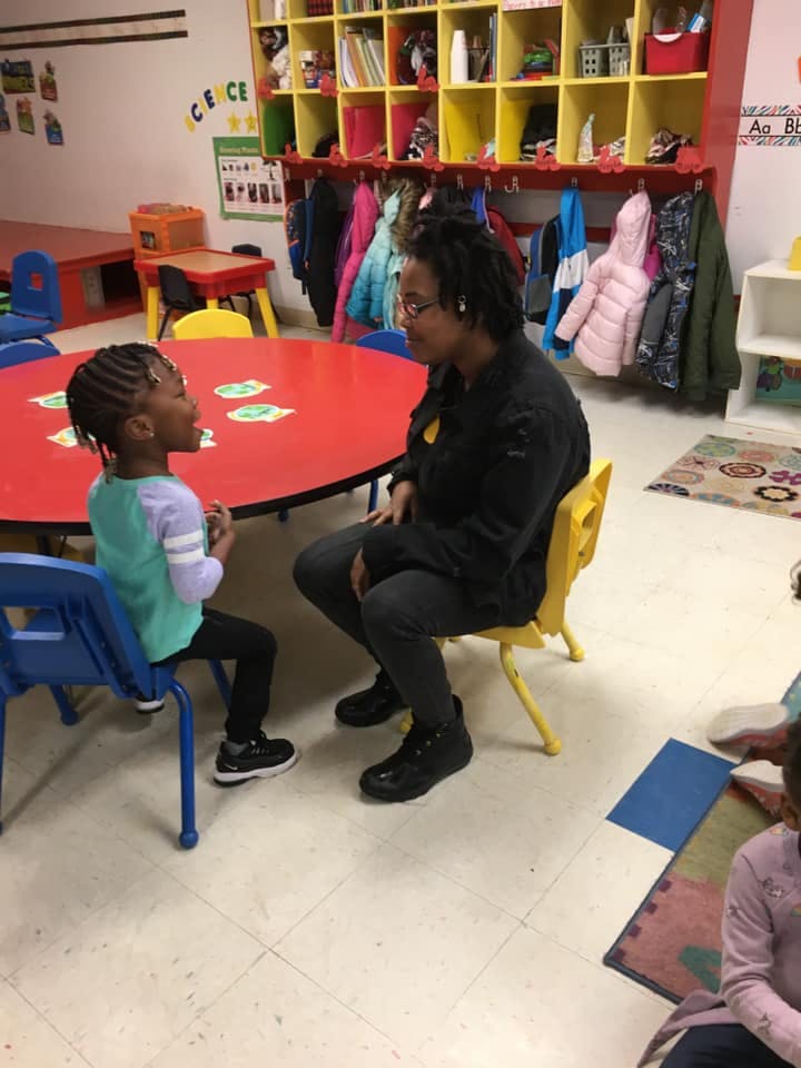 Person and child sitting at a red table in a classroom