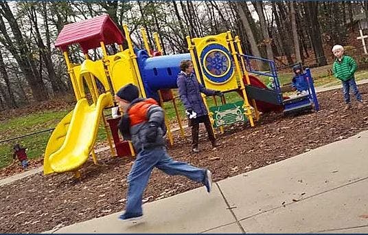 Child running on playground with other children and play structure
