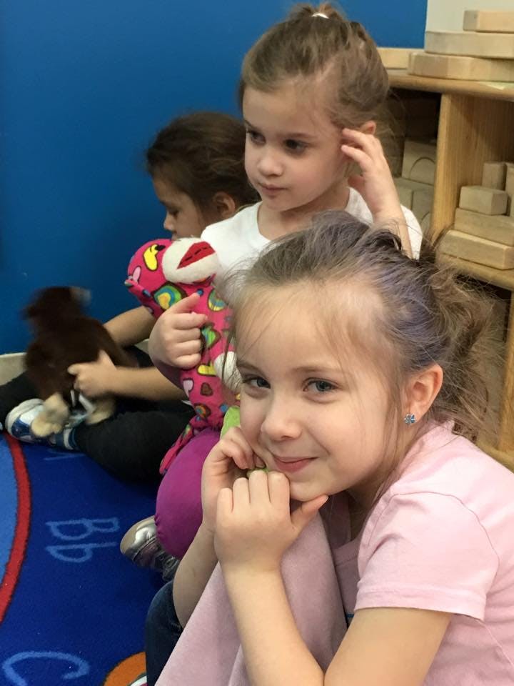 Three children sitting on the floor, one holding a stuffed animal