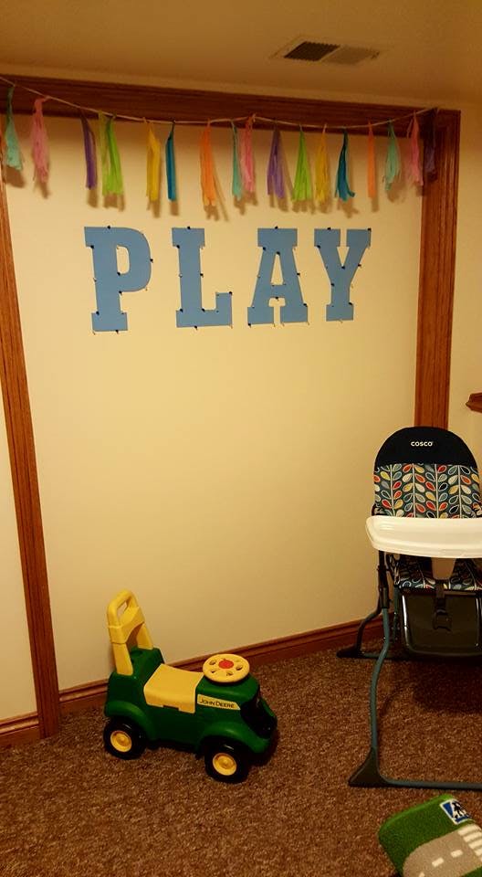 Wall decor with the word PLAY, a ride-on toy, and a high chair