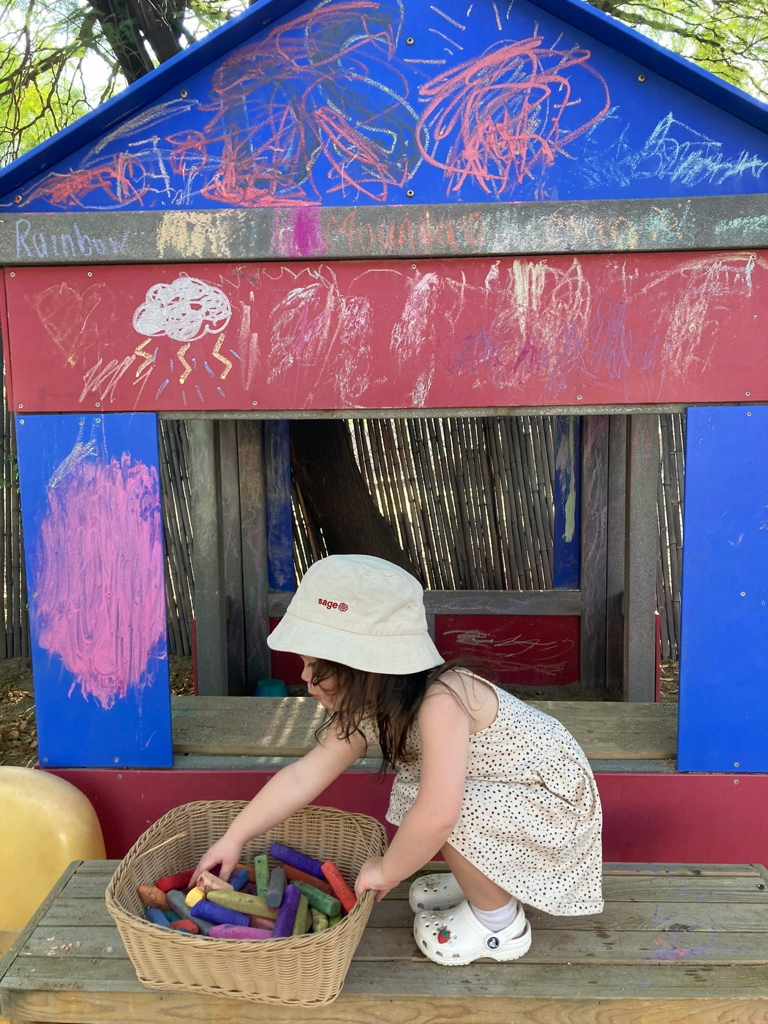 Child in a hat reaching into a basket of colorful blocks