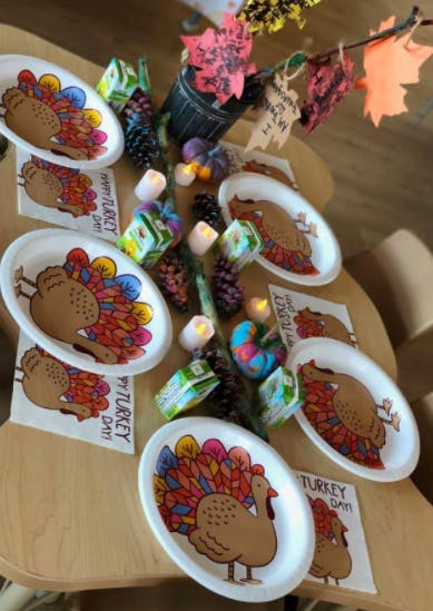 Table set with turkey-themed paper plates and napkins, pinecones, and candles