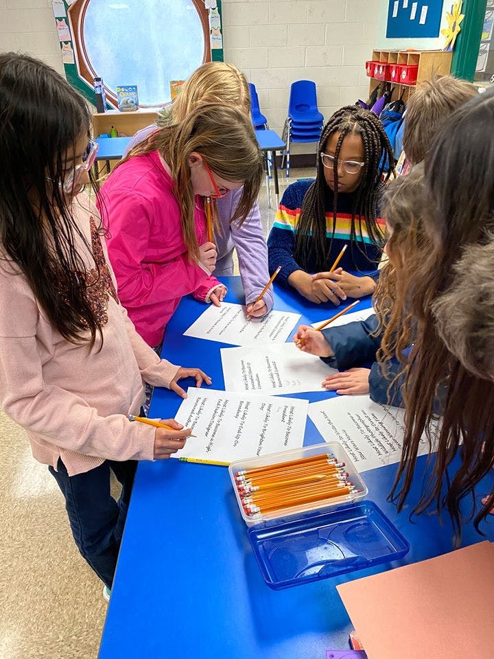 Children writing on papers at a blue table in a classroom