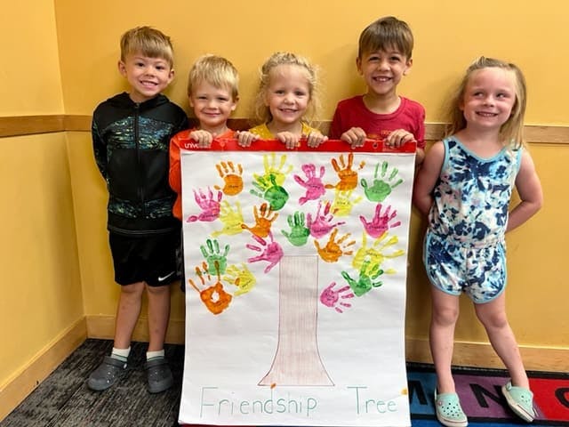 Five children holding a poster of a handprint tree with "Friendship Tree" written below