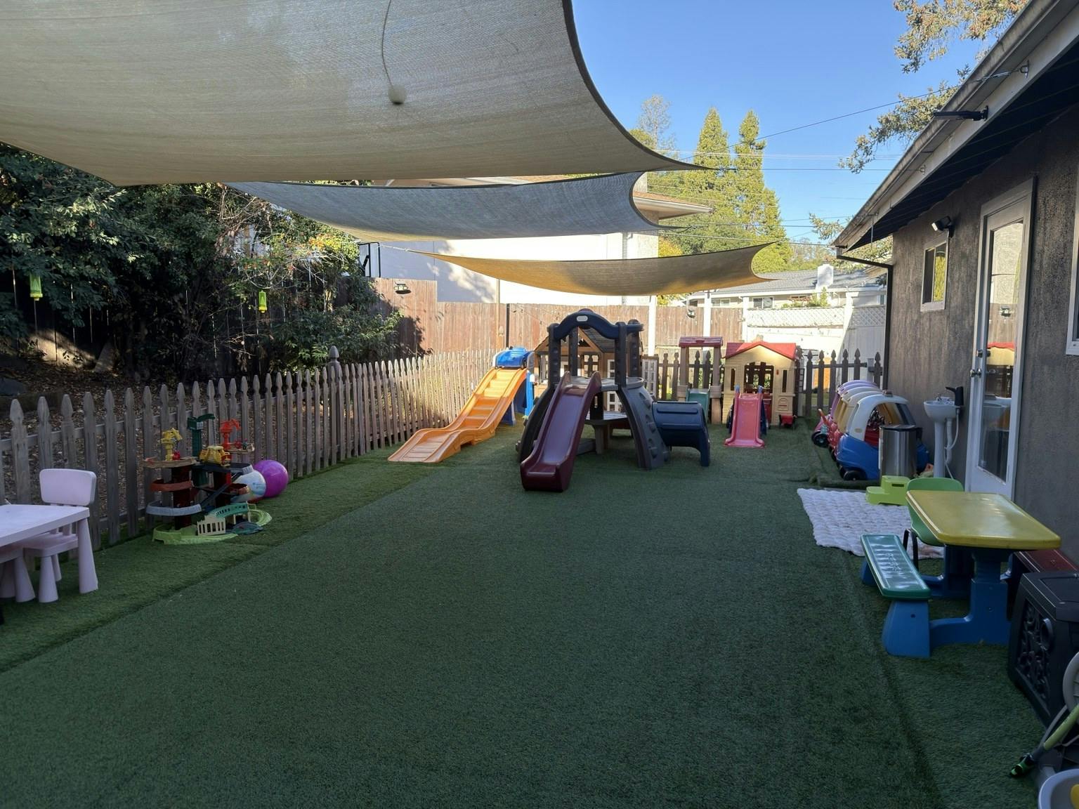 Playground equipment and tables on artificial turf in a fenced yard