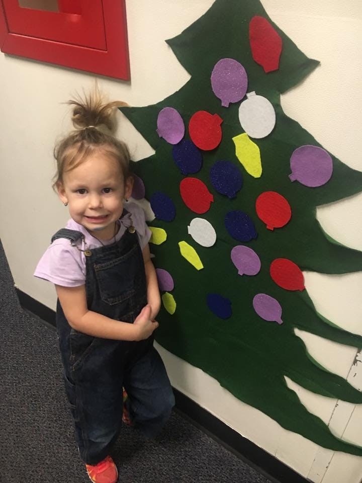 Child standing next to a felt Christmas tree with colorful ornaments