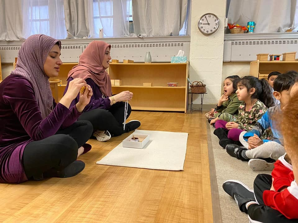 Two people in hijabs demonstrating to a group of children in a classroom