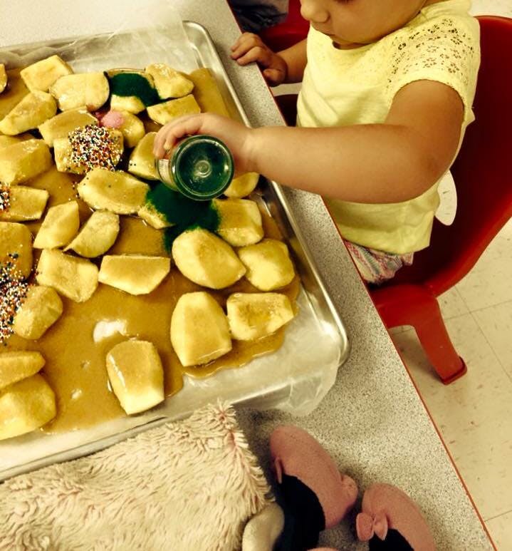 Child pouring green liquid onto food on a tray