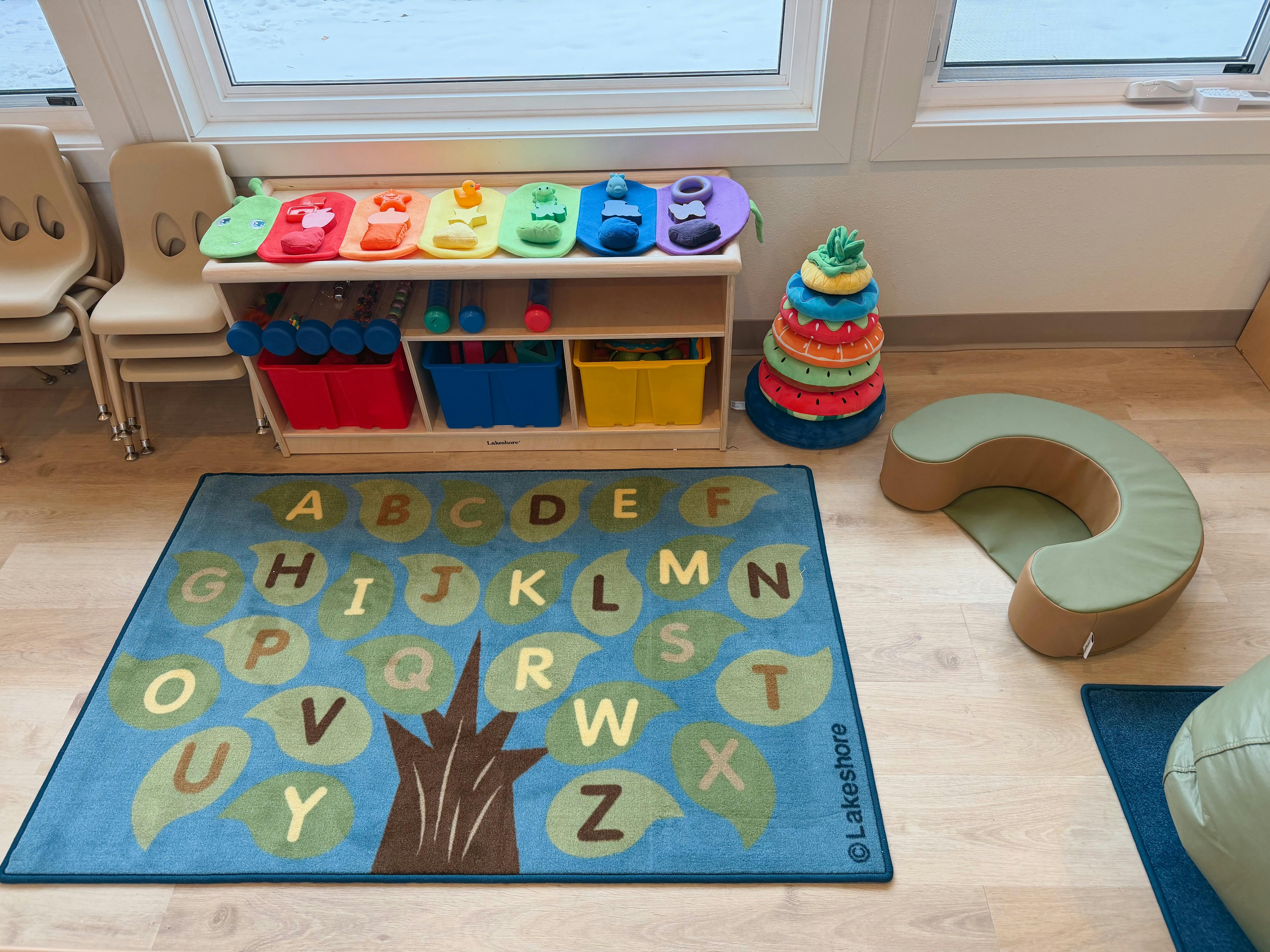 Classroom with an alphabet rug, cubby shelf, small chairs, and soft play items