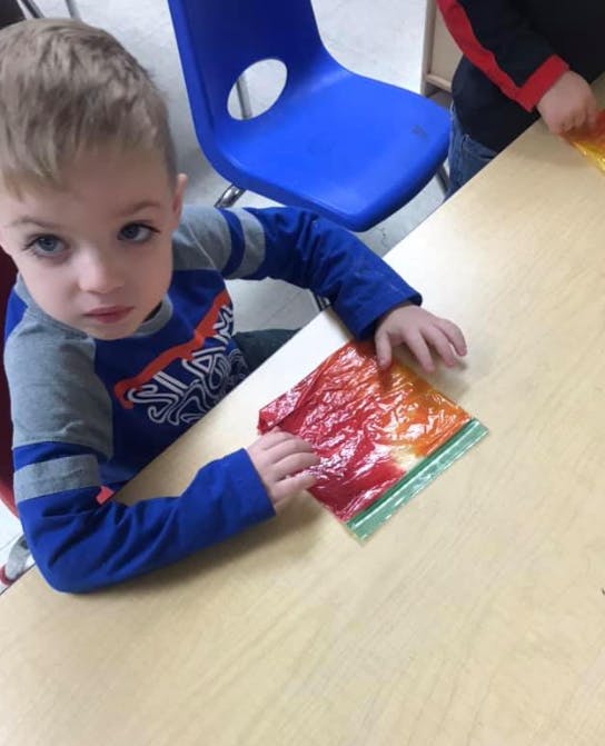 Child at a table holding a colorful plastic bag