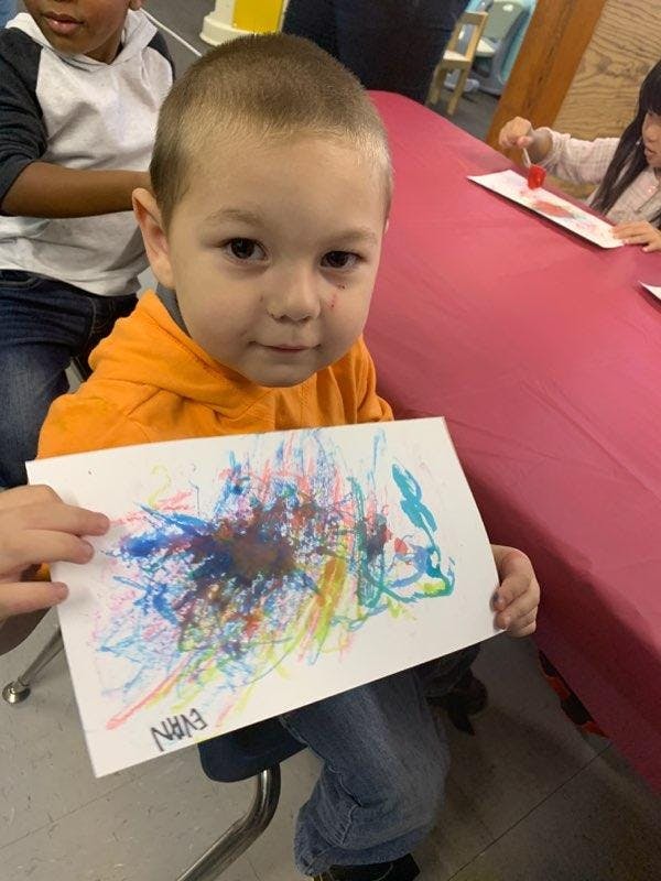 Child holding up a colorful abstract drawing