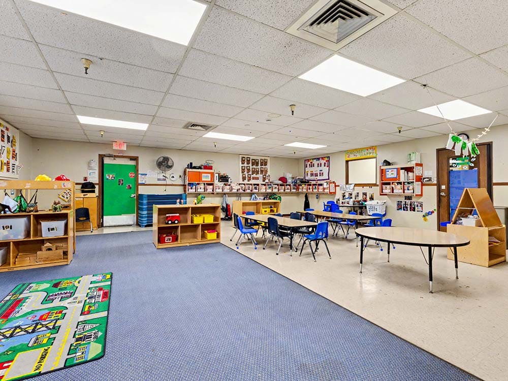 Empty classroom with children's tables, chairs, and shelves of toys