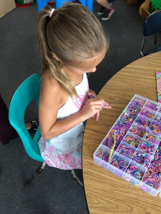 Child sitting at a table with a container of colorful rubber bands