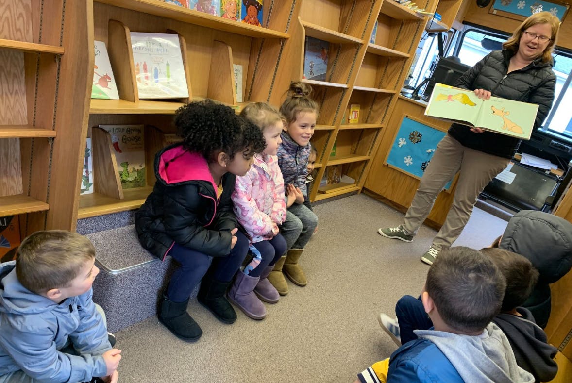 Adult reading a book to a group of children in a library