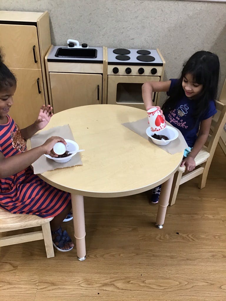 Two children at a table with bowls and cups in a play kitchen area