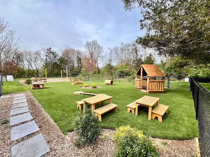 Outdoor play area with artificial turf, picnic tables, playhouse, and log tunnel