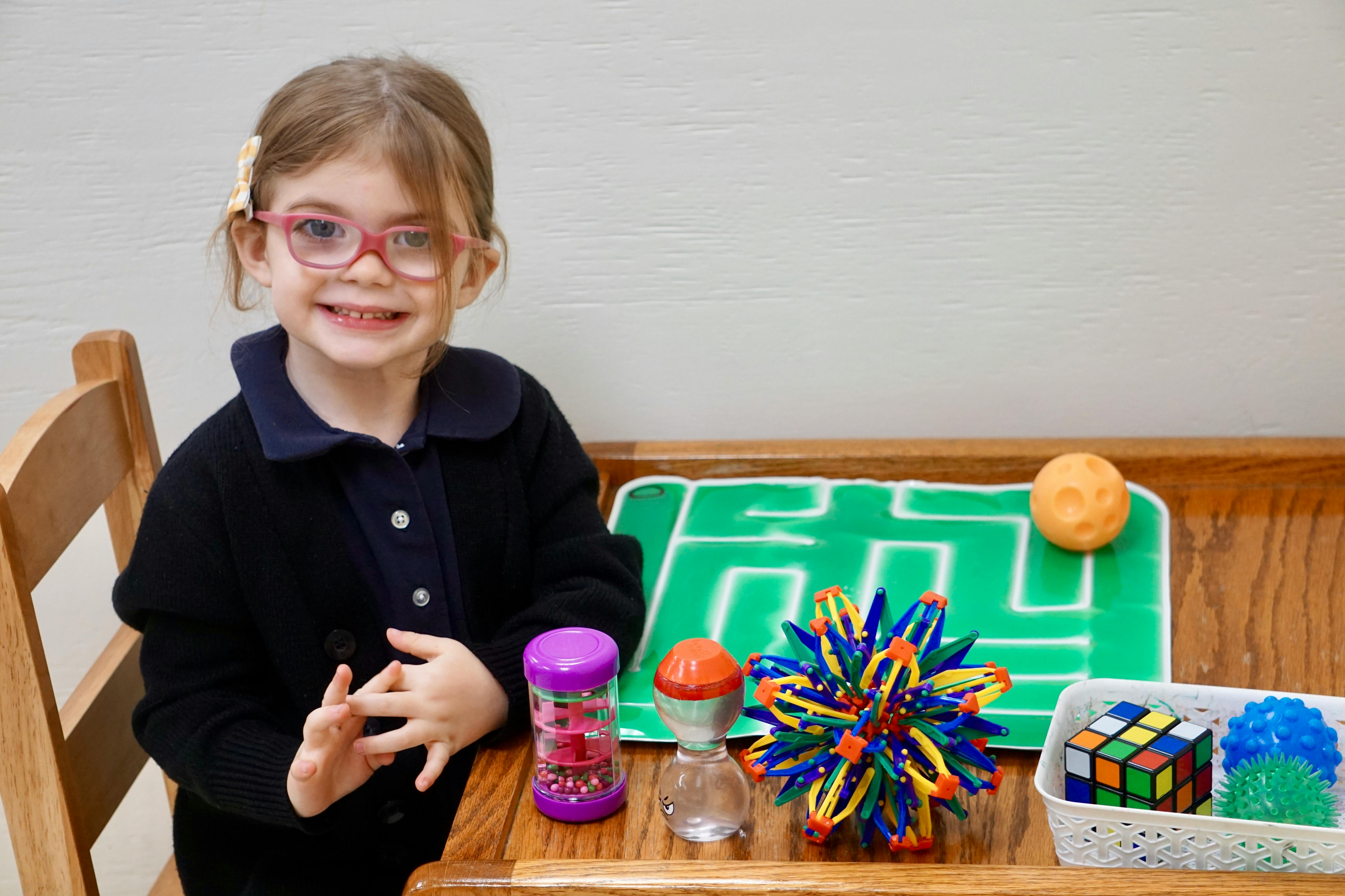 Child with glasses sitting at a table with sensory toys
