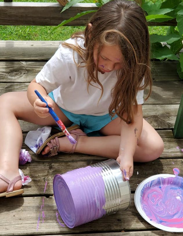 Child painting a metal can purple