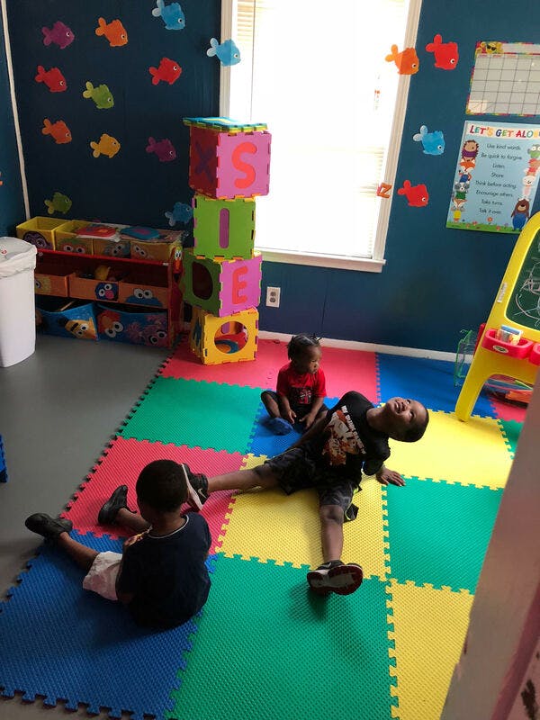 Three children sitting and lying on a colorful mat in a playroom