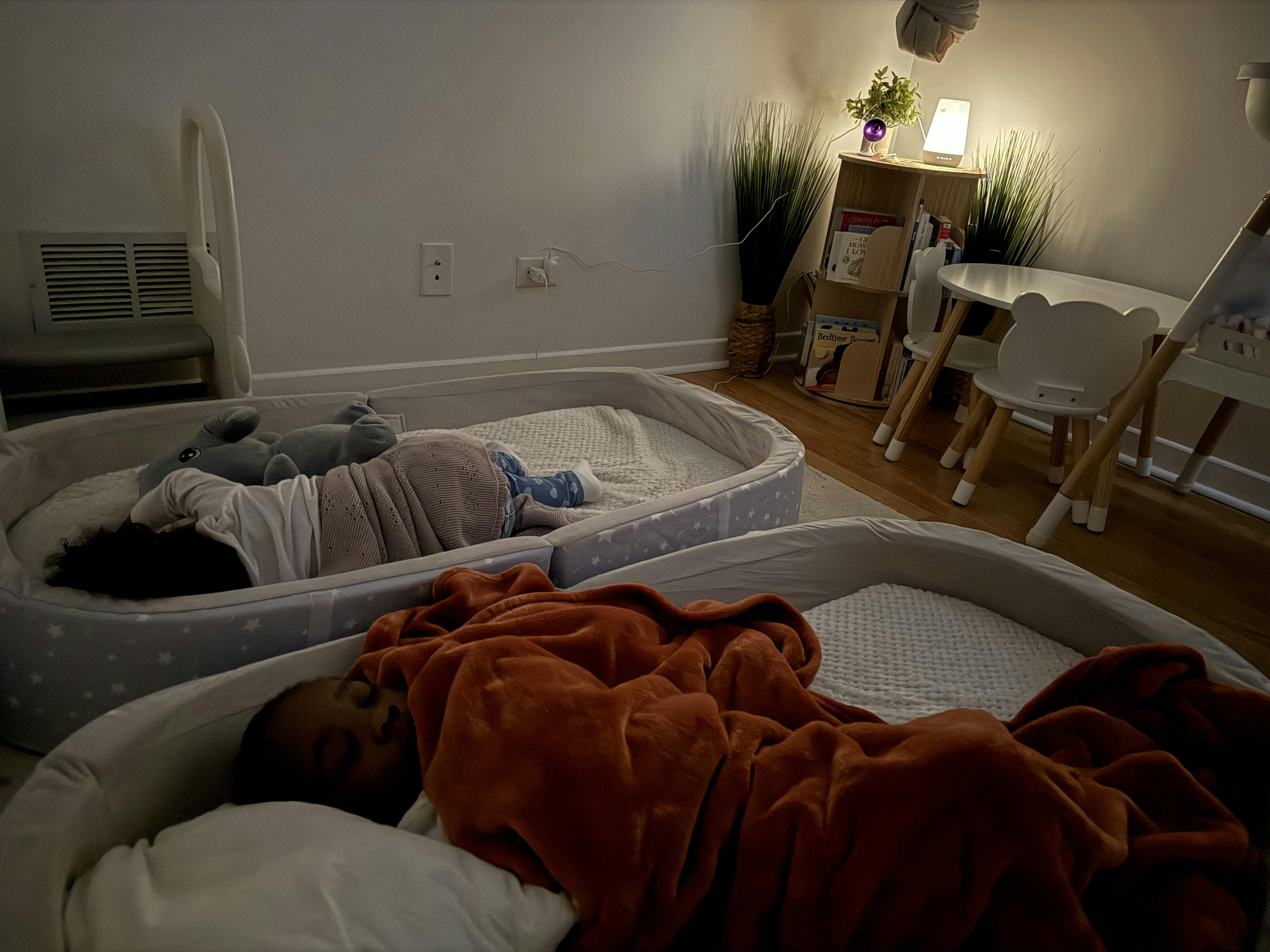 Two children sleeping in separate beds on the floor