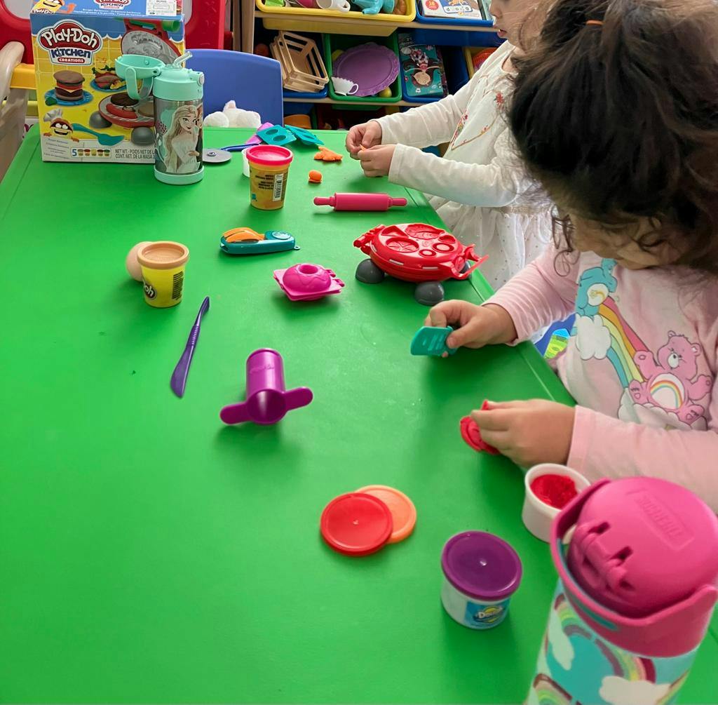 Children playing with colorful playdough and tools on a green table