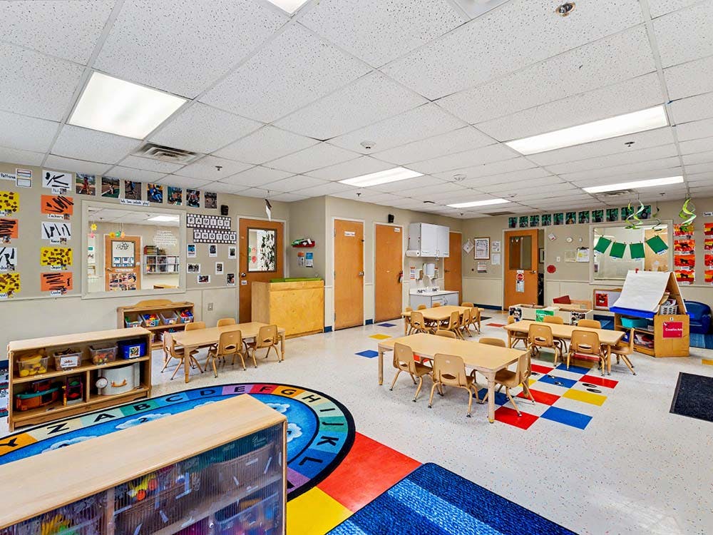 Empty preschool classroom with small tables, chairs, and colorful rug