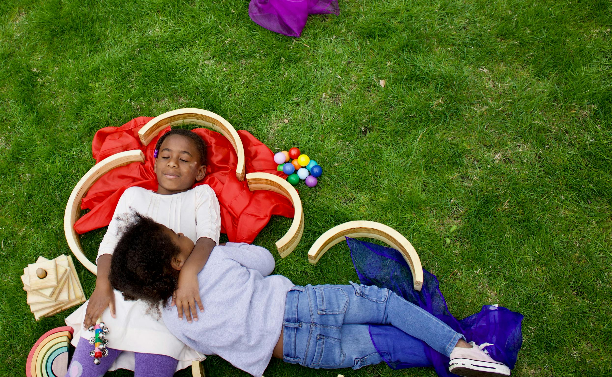 Two children lying on grass with toys