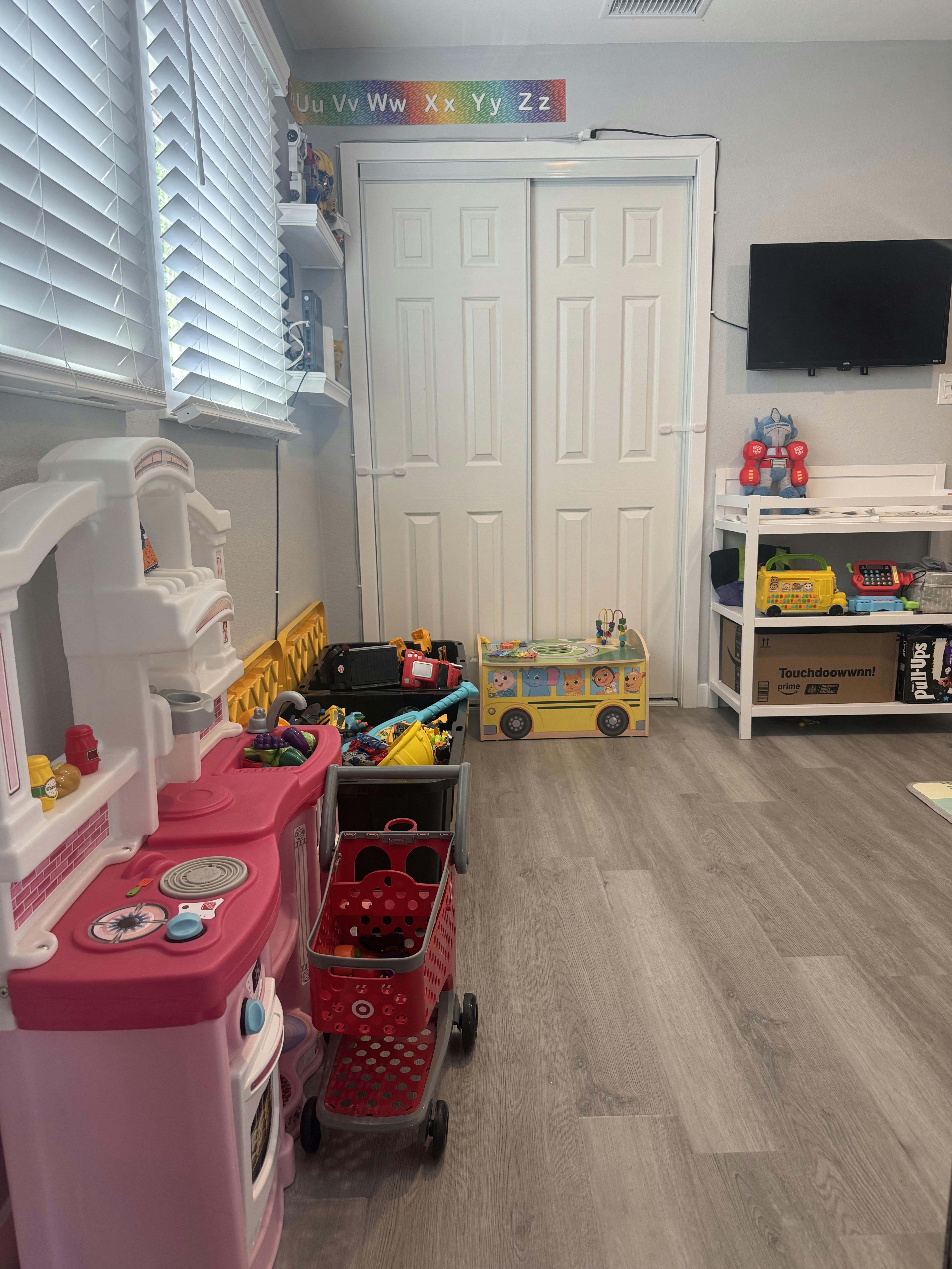 A playroom with various toys, including a play kitchen, shopping cart, and toy bus
