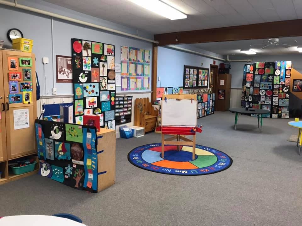 Classroom with children's artwork on walls and an easel on a colorful rug